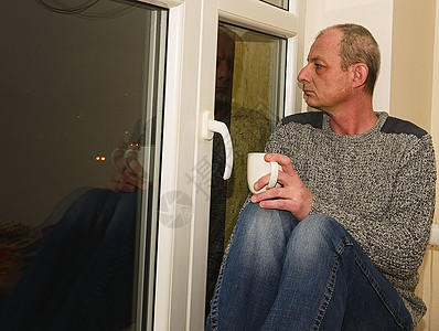 坐在窗户旁边的中年压抑男子 他喝着咖啡药品成人医生窗台孤独压力病人悲哀寂寞男人图片