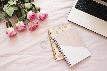 粉红色床单上的笔记本 膝上型电脑 一束玫瑰花 平躺风格的自由时尚家居女性气质工作区图片