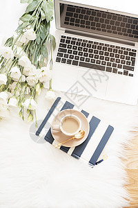 白色毛皮地毯上的地板上有笔记本 笔记本电脑 一杯咖啡和一大束白花 自由时尚舒适的女性家庭工作区 平躺风格 顶视图 条纹和金色图片