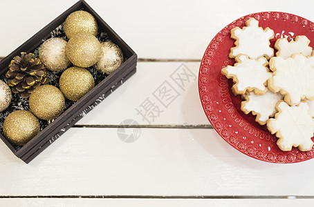 金色圣诞球装在木箱里圣诞饼干在白色质朴的木制背景上的红色托盘中呈雪花状 顶视图复制空间图片
