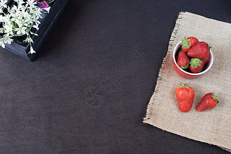 草莓特写海珊黄麻上的迷你金属桶里的新鲜草莓 装饰木箱中的白花和紫花 黑色背景背景