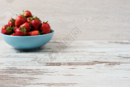 模糊效果背景 一堆多汁的成熟有机新鲜草莓放在一个大蓝色碗里 轻质朴的木制背景图片