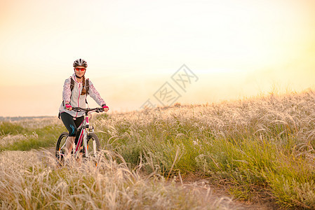 年轻女子在日落 冒险和旅行的青春草原上骑着山地自行车跑运动山地车女士地平线天空运动员羽毛车轮场地娱乐图片