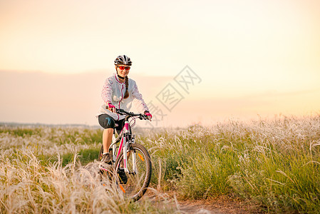 年轻女子在日落 冒险和旅行的青春草原上骑着山地自行车跑头盔行动运动员地平线运动女性女士娱乐车轮羽毛图片