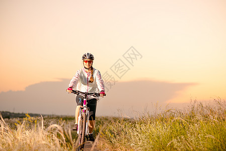 年轻女子在日落 冒险和旅行的青春草原上骑着山地自行车跑娱乐天空女士运动员头盔女性羽毛行动运动场地图片
