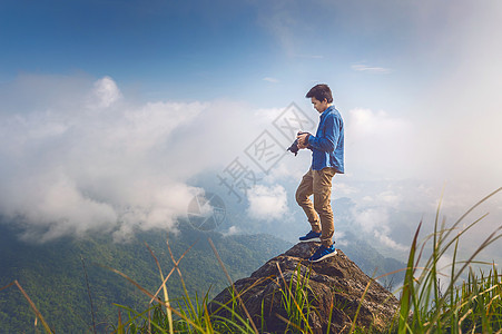 摄影师手握着摄像机 站在自然中的岩石顶上 旅行概念 古老的语气太阳相机远足者背包三脚架砂岩工作男人照片日落图片