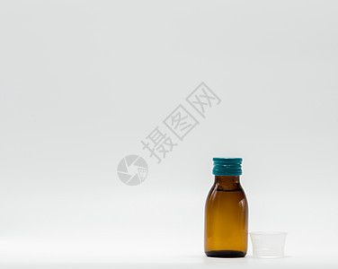 含白标签和白色底底面塑料测量杯的琥珀瓶中的抗热糖浆图片