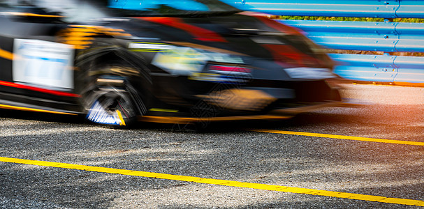 赛车在有蓝色篱芭和黄线交通标志的柏油路的赛车 汽车行驶速度快 运动模糊 带有红色和黄色条纹的黑色赛车 赛道上的汽车图片