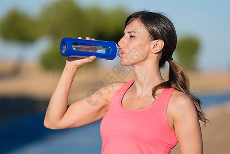 运动服装中漂亮女孩的侧面景色 在公园锻炼后喝着饮用水图片