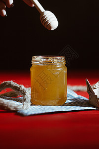 玻璃罐中的蜂蜜紧靠在红色木桌上的黑色背景上 用棒状蜂蜜勺倒蜂蜜养蜂业花朵蜂蜡甜点勺子厨房美食玻璃木头糖浆图片