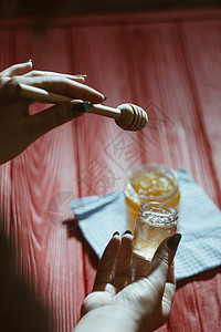 玻璃罐中的蜂蜜紧靠在红色木桌上的黑色背景上 用棒状蜂蜜勺倒蜂蜜集装箱美食生物厨房营养蜂蜡食物玻璃桌子产品图片