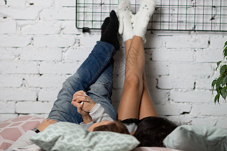 一个年轻男人和他的女朋友躺在床上 将他的脚扔在白砖墙上的石墙上说谎休息女性房子成人冥想瑜伽电话房间睡眠图片