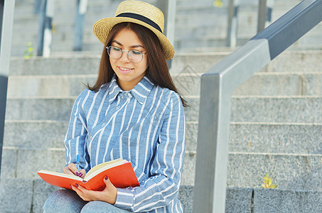 一名戴眼镜的亚洲青年学生身穿蓝条纹衬衫戴顶帽子的肖像眼镜快乐幸福女性楼梯笔记本微笑女孩大学技术图片
