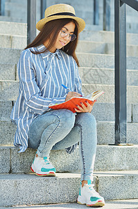 坐在台阶上并写在笔记本上的亚洲年轻女孩青少年楼梯成人城市微笑学生大学快乐牛仔裤喜悦图片