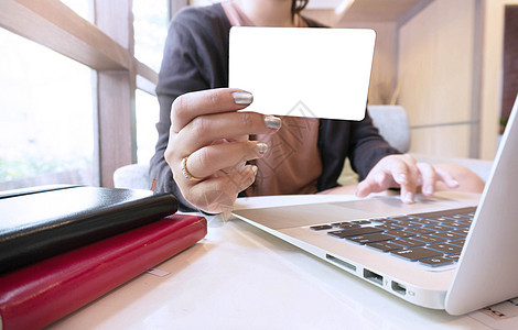 年轻女性手持塑料信用卡和使用笔记本电脑图片