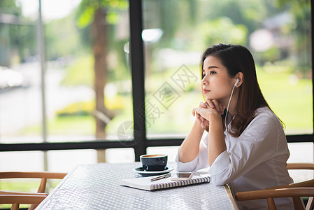 美丽的女孩在咖啡厅里听音乐 喝点咖啡店铺职场桌子学生互联网大学办公室商业学校写作图片