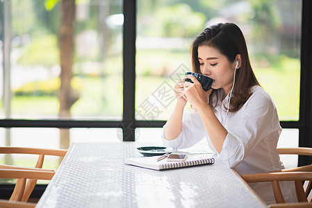 美丽的女孩在咖啡馆工作 喝咖啡和咖啡写作杯子店铺餐厅学校教育电脑技术人士学生图片
