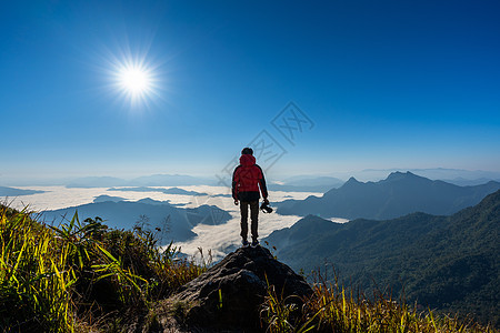 摄影师手持照相机 站在自然中的岩石顶端 旅行概念 笑声天空背包照片镜子冒险阳光艺术家顶峰工作摄影图片