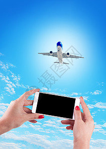 飞机拍摄使用移动电话和飞机在蓝色面包上持有女性手的通讯器商业手指客机细胞航空技术女士触摸屏电子背景