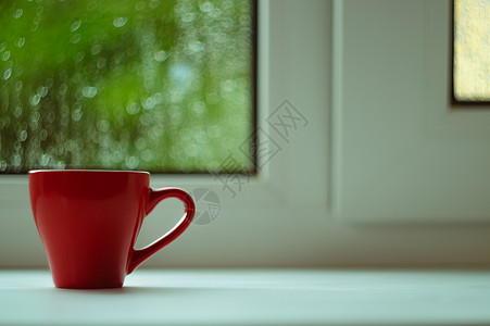 白色窗台上的红咖啡杯 背景窗口和雨中 杯子位于边框左侧中心绿色咖啡窗户红色太阳图片