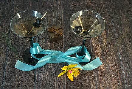 两杯配橄榄的马提尼杯 有蓝丝带 黄色兰花和木制桌上的礼品盒餐厅酒吧假期邀请函季节木头玻璃念日风格桌子图片