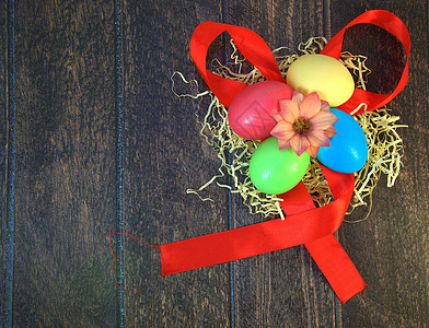 四个漆成复活节的鸡蛋在稻草巢中 中间有一朵花 躺在木制桌子上的红色丝带上刷子假期手工丝带庆典丝绸海报蓝色传统季节图片