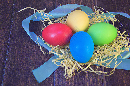 一张蓝丝带上的稻草巢中彩绘的复活节彩蛋躺在一张木桌上季节假期风格乡村磁带装饰食物传统团体横幅图片