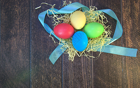 一张蓝丝带上的稻草巢中彩绘的复活节彩蛋躺在一张木桌上桌子海报季节传统乡村假期庆典横幅休息日装饰图片