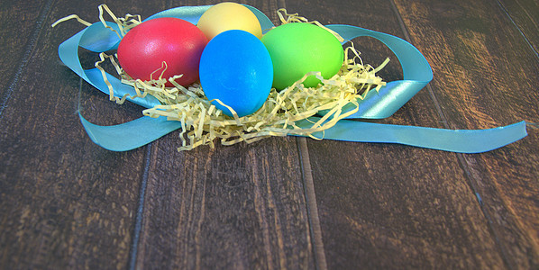 一张蓝丝带上的稻草巢中彩绘的复活节彩蛋躺在一张木桌上乡村横幅食物海报休息日装饰季节团体磁带庆典图片