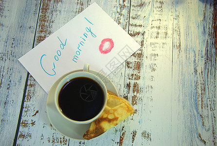 早安咖啡茶碟上的一杯咖啡 新鲜出炉的煎饼和一张写着早安心愿并涂了一丝口红的纸恋爱杯子桌子早餐金子食物飞碟贴纸厨房陶瓷背景