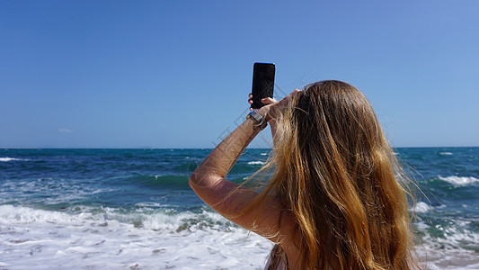 使用移动电话 海滩和海背景的近身检查一名女性海洋蓝色娱乐技术商业旅行天空屏幕冒险互联网图片