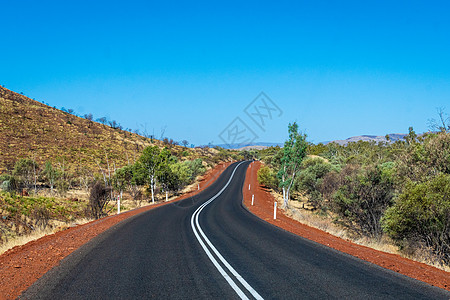 澳大利亚Karijini国家公园山丘之间有深薄油塔的黑暗公路图片