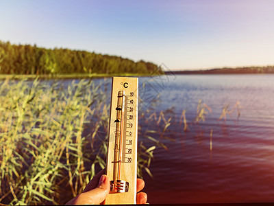 显示 30 摄氏度热量的温度计以湖水和蓝天为背景在阳光下海浪预报蓝色高温状况海滩环境热带太阳天气图片
