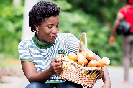 扶着年轻女人的女青年在大腿上拿着一篮子食物绿色黄色大车女性微笑水果香蕉生食橘子图片