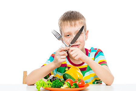 拿着刀和叉子的男孩 吃新鲜生蔬菜 肖像图片