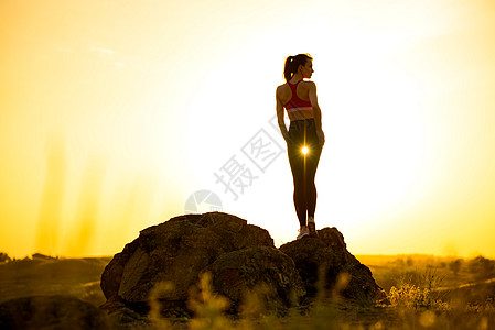 年轻女子站在岩石上 在热辣的美丽夏日 冒险和健康活跃生命轮概念 笑声练习日落女性耀斑阳光成人沉思天空镜片运动图片