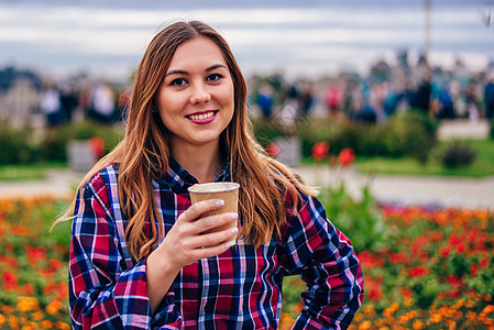 美丽的年轻女士拿着咖啡杯和微笑着笑容饮料女孩女性杯子公园快乐日落头发衬衫咖啡图片
