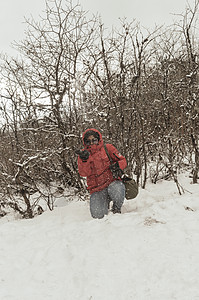 一个穿着红色套头夹克的女人微笑着快乐地享受着第一场雪的玩耍和向空中扔雪球的肖像 在冬天享受下雪天的景色 农村查谟和克什米尔暴图片