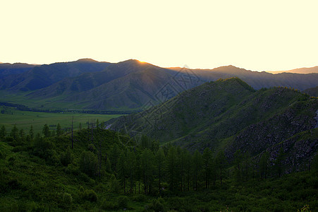 夜晚的风景 日落的太阳隐藏在高山后面 用光线照亮了闪烁的山谷图片