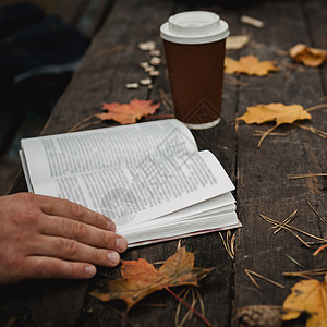 男性女性在秋季公园看书喝外卖咖啡 特写在肩膀上 模糊 顶视图 节省空间 见过手 深色复古风格文学日记自由学生小说故事橙子毛衣图书图片