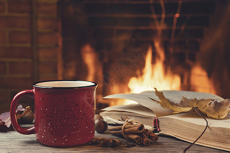 红色大气红杯加热茶和一本开着的书 在燃烧的壁炉 舒适 放松和温暖的心房概念面前柠檬咖啡火焰饮料照片房间季节假期桌子烧伤背景