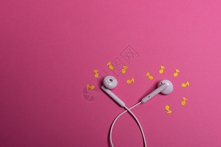 粉红色背景上的白色耳机和黄色纸币 从上面看笔记文化耳朵工作室立体声创造力水平粉色金属电子图片