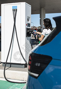 妇女对加油站的电动汽车充电 蓝色汽车和电动汽车收费细胞充电器机动性能源电池力量加载电气绿色图片