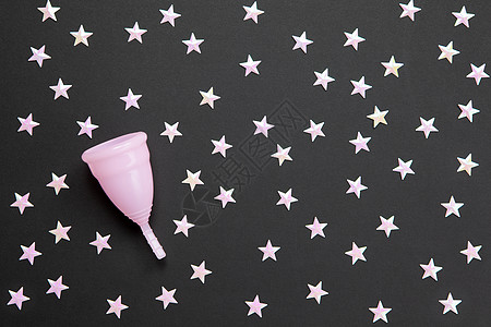 黑色背景上有无数星星的粉红色月经杯 晚上使用杯子的概念可能性 零浪费 储蓄 极简主义 女性卫生用品 平躺 复印空间 水平的图片