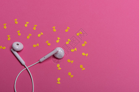 粉红色背景上的白色耳机和黄色纸币 从上面看立体声配饰工作室文化创造力耳朵电缆电子电话金属图片