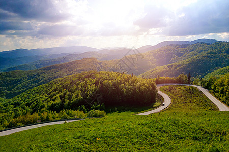 横穿森林的弯曲道路阳光运输高山石头天空爬坡全景土地草地旅行图片