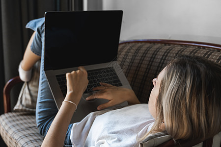 一台笔记本电脑躺在沙发上的女人 在线学习和工作 自由职业者 个体户女性 女孩在沙发上用笔记本工作 桌上放着电话 智能手机和电子阅图片