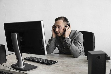 穿着衬衫的年轻商务人士或学生戴着耳机坐在电脑显示器前 通过互联网与某人交谈 给他们留下了快乐的微笑印象深刻 在办公室的桌子上使用图片