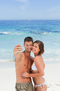 爱人和他们的相机在沙滩上旅游热带袖珍旅行女士快乐姿势拥抱摄影拍照背景图片