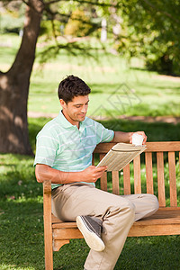 男人在看报纸幸福游戏男性长椅杯子闲暇填字绿色公园绿色植物图片